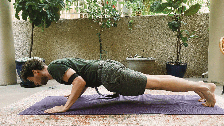 Man practicing Chaturanga, or a half push-up, with a strap around his upper arms