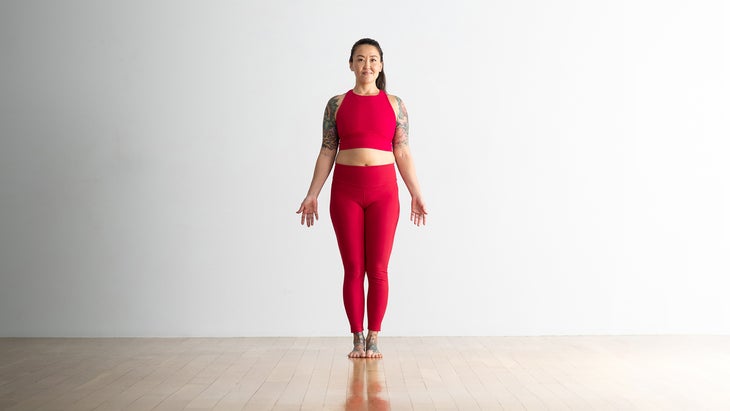 Woman standing on her yoga mat in Mountain Pose, or Tadasana, with her feet together and her arms alongside her body