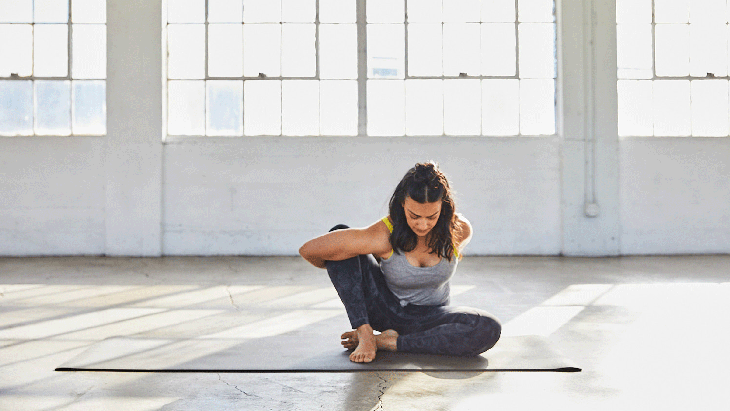Woman sitting on a yoga mat with her right knee bent in a modification of Lotus Pose