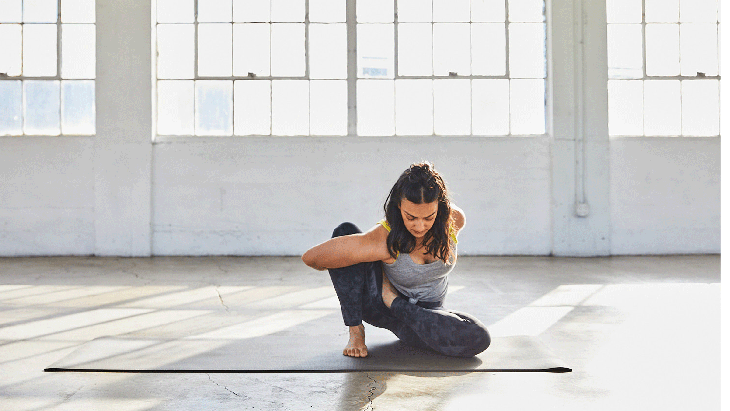 Woman sitting on a yoga mat with her right knee bent and her left heel by her right hip in a modification of Lotus Pose