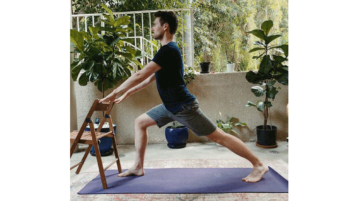 Man standing on a yoga mat in front of a chair with his hands on the back
