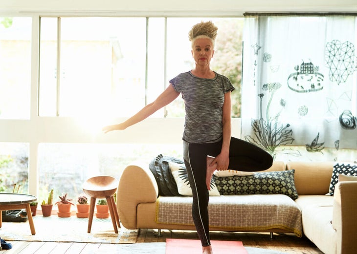 Woman standing in her living room practicing Tree Pose in Yoga