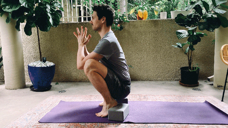 Man in a yoga squat, or Malasana, with blocks beneath his heels for support