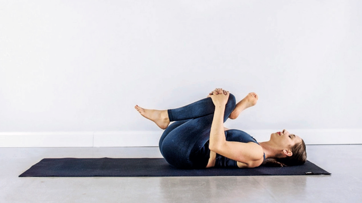 Kassandra Reinhardt reclining on a yoga mat in a figure-4 shape while practicing Yin Yoga for the new Moon