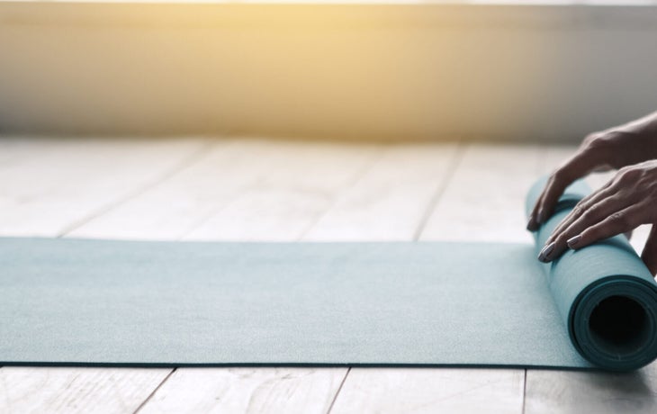 Woman unrolling a yoga mat on a hard wood floor in a yoga studio