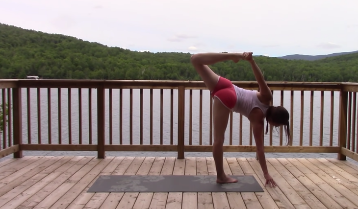 Yoga With Kassandra seated cross-legged outside on a mat practicing a side stretch during Half Moon Pose