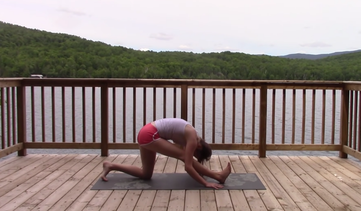 Yoga With Kassandra practices half split on a mat while outside