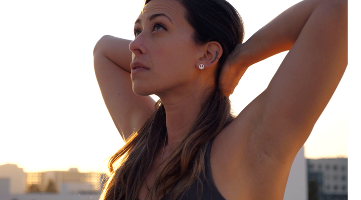 Woman practicing Chair Pose in yoga with her fingers interlaced behind her head and her back arched in Cow Pose