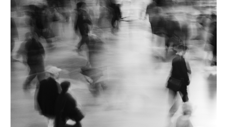 Black-and-white photo of a crowded sidewalk with blurred images of people rushing